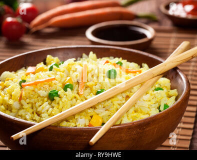 Cooked white rice with curry and vegetables in a bowl with sauces and chopsticks on a wood brown bamboo background. Stock Photo