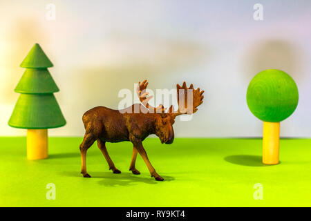 Toy elk in a toy forest. like a real moose on a bright studio background with wooden trees.Eco toys. Stock Photo