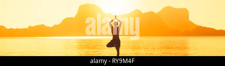 Man stands on the beach next to rocks, practicing yoga during amazing sunset over the sea Stock Photo