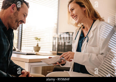 Female doctor showing good test results to a male patient. Smiling medical professional sharing good test results with her patient. Stock Photo
