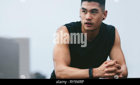 Muscular asian man standing outside and looking away. fitness male model in sports clothing resting after his workout. Stock Photo