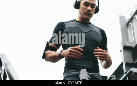 Asian man moving down the stairs as a part of exercise routine. Young man in sports clothing with headphones working out outside on steps. Stock Photo