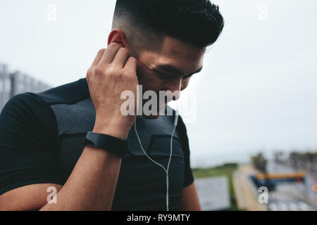 Close up of young asian man in sportswear wearing earphone to listen music during outdoor training.
