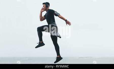 Sporty asian man doing intense exercises. Side view of fitness male exercising jump and lunge. Stock Photo