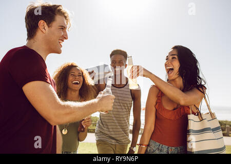 Group of multi-ethnic friends having beers while walking to the picnic spot. Men and women friends going on a picnic on a summer day. Stock Photo