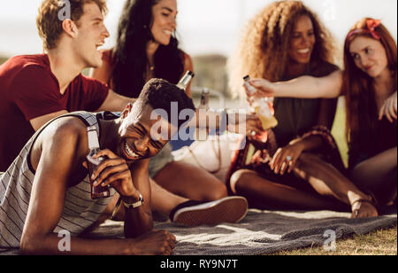 Cheerful young african guy sitting with friends outdoors and laughing. Man enjoying summer weekend with friends. Stock Photo