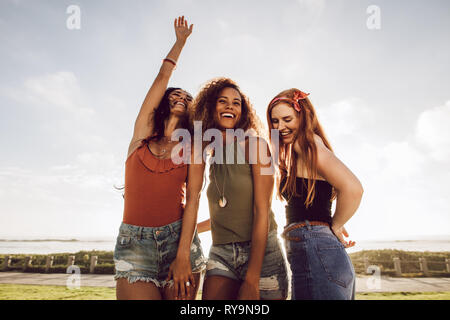 Group of three young women standing outdoors and dancing. Beautiful female friends having a great time on their summer vacation. Stock Photo