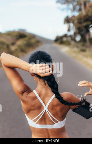 Rear view of fitness woman tying hair before her training session outdoors. Young woman getting ready for running workout. Stock Photo