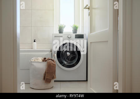 Washing machine in modern light bright bathroom. Laundry bag with towels near it. Scandinavian hygge style interior Stock Photo