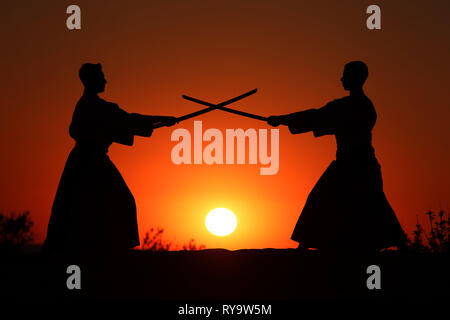 Silhouettes of two warriors on the beach at sunset with crossed fighting swords Stock Photo