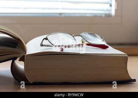 Open book on a table with reading glasses Stock Photo