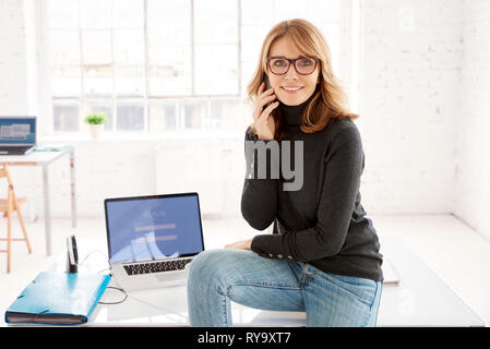 Shot of middle aged businesswoman using her mobile phone and making a call while standing in the office. Stock Photo