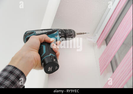 Installing fabric roller blinds. A man fixes basis blinds to frame the window. Stock Photo