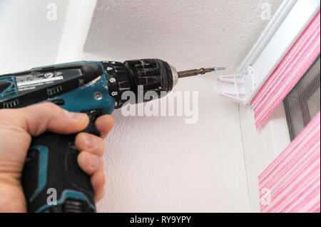 Installing fabric roller blinds. A man drilling holes to fix basis blinds. Stock Photo