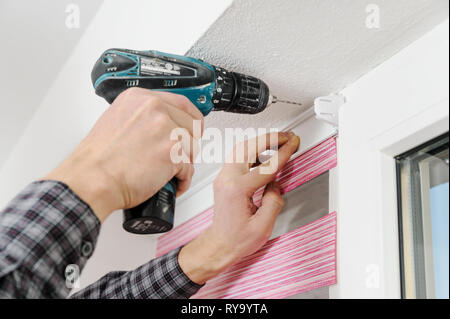 Installing fabric roller blinds. A man drilling holes to fix basis blinds. Stock Photo