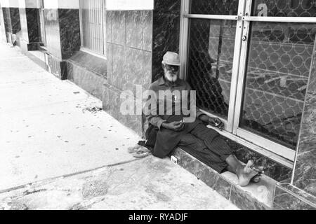 Port of spain, Trinidad and Tobago - November 28, 2015: old bearded man african American hobo or homeless sitting at building window in street outdoor Stock Photo