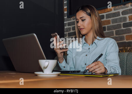 Female graphic designer working with laptop and using smartphone. - Image Stock Photo