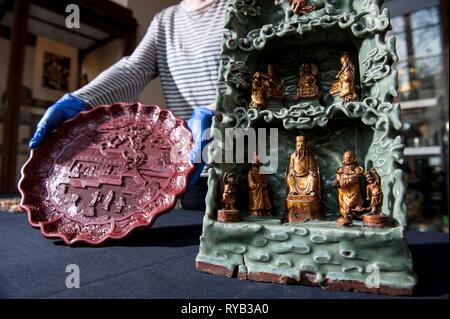 The objects featured :   -carved red lacquer on wood core   1403-24 features scenes of Imperial Household  35 cm diameter.   - one pair of gold pillow ends probably made for a member of the Ming royal family   - Longquan shrine - stoneware celadon glazing and gilding Tongle era 1406 . at the top supreme Daoist god of thunder rides mythical beast called a qilin  middle niche are the Three Pure Ones Gods who encapsulate Daoist philosophy . In the centre Celestial   Worthys . In the centre visible in the reverse shot is is the CW of Promordial Being . In the lower grotto are the Jade Emperor  cen Stock Photo