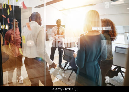 Diverse group of smiling businesspeople talking and laughing together after a meeting in a bright modern office Stock Photo