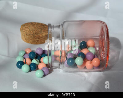 A glass jar of push pins photographed on a white background from a side angle, on its side with push pins split out and lid by the side Stock Photo