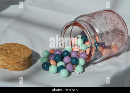 A glass jar of push pins on its side with push pins split out and the lid next to it Stock Photo