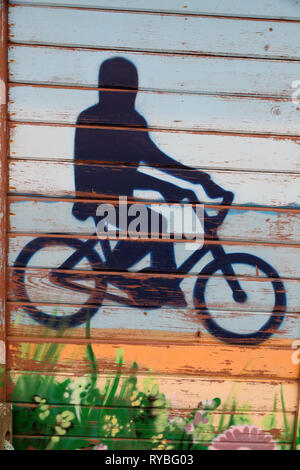 Graffiti on a wooden wall about a man riding a bicycle near the sea Stock Photo