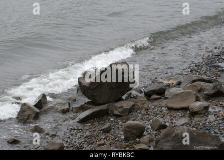 Incoming wave on shoreline with large boulder Stock Photo