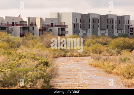 Brown water after heavy rains flows by apartment buildings next to river on sunny day Stock Photo