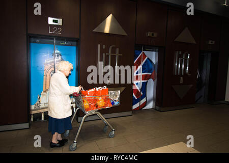 Lady shopping in the Grosvenor Centre with shopping trolley leaving Sainsburys Supermarket with trolley union Jack All Saints Church Northampton flag Stock Photo