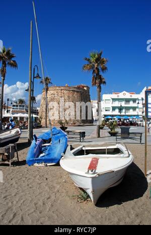 Small boats on the beach with the old watch tower and pavement cafes to the rear in the Plaza de Torreon, La Cala de Mijas, Malaga Province, Andalusia Stock Photo