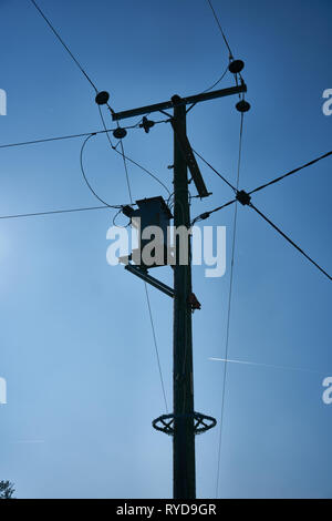 Silhouette of a wooden electrical power distribution post and overhead cables against a blue sky. Stock Photo
