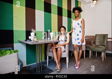 Two black african girlfriends at summer dresses with milkshake cocktails at cafe. Stock Photo