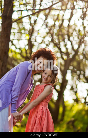 Portrait of a smiling mid adult woman and her daughter holding hands while standing in a forest. Stock Photo