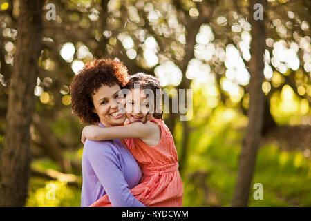 Portrait of a mid adult woman and her young daughter hugging in a forest. Stock Photo