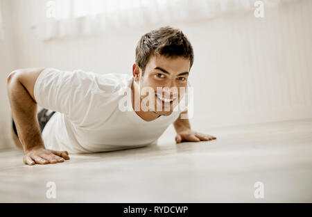 Portrait of a smiling young man doing push-ups inside a room. Stock Photo