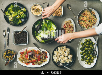 Vegan dinner table setting. Healthy vegetarian dishes in plates on table. Flat-lay of vegetables, legumes, beans, olives, sprouts, hummus, couscous an Stock Photo