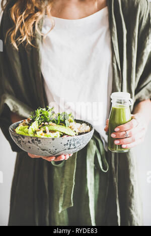 Healthy dinner or lunch. Woman in linen shirt standing and holding vegan superbowl or Buddha bowl with hummus, vegetable, fresh salad, beans, couscous Stock Photo