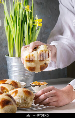 Child hands take homemade Easter traditional hot cross buns on cooling rack on white marble table with narcissus flowers. Stock Photo