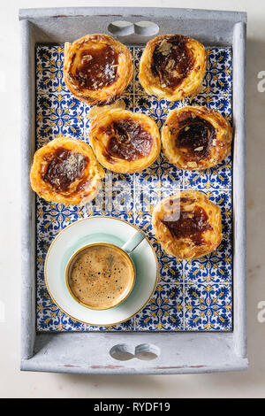Traditional Portuguese egg tart dessert Pasteis Pastel de nata in classic tile tray with cup of black coffee. Flat lay, space Stock Photo
