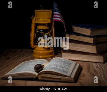 Stacked vintage books closed on a desk with an old yellow German lamp, a pipe and an american flage - classic litereracy concept Stock Photo