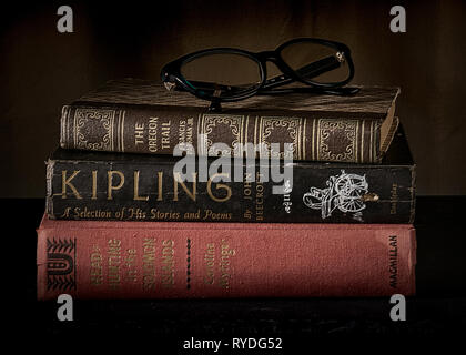 Three stacked vintage classic books closed on a desk with reading glasses on top - classic litereracy concept Stock Photo