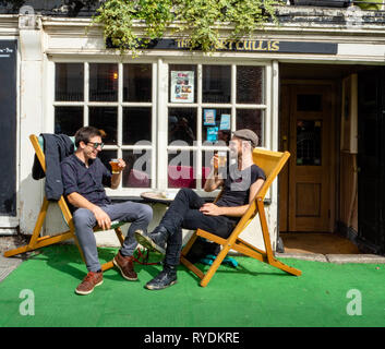 Friends enjoying a beer in the deckchairs outside the Portcullis a local real ale pub in Clifton village Bristol UK Stock Photo