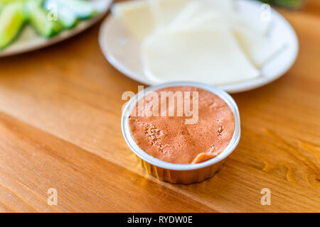 Wooden table setting of healthy vegan vegetarian lunch with container package of pate spread and cheese slices with cucumbers in home Stock Photo