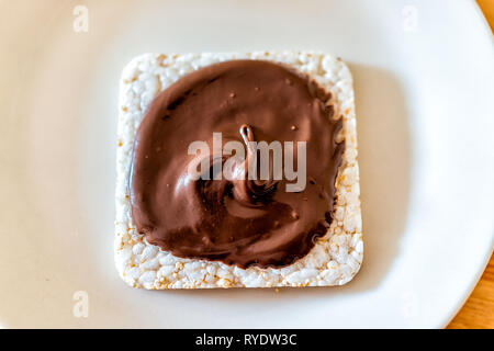 Flat top closeup of rice cake with chocolate hazelnut spread with brown sauce or syrup vegan vegetarian snack dessert one single piece on white plate Stock Photo