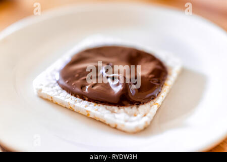 Closeup side of rice cake with chocolate hazelnut spread with brown sauce or syrup vegan vegetarian snack dessert one single piece on white plate Stock Photo