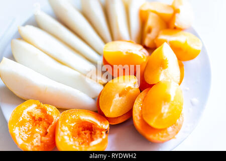 Closeup of cut fruit pear or apple slices and apricot plum halves on white plate macro and orange yellow vibrant color snack Stock Photo