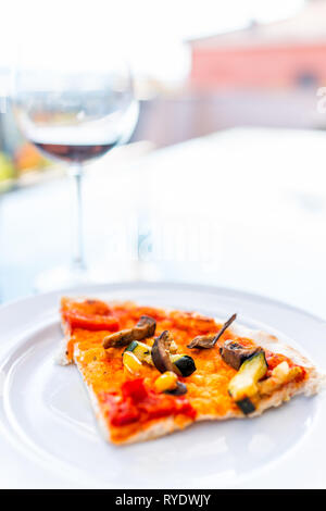 Closeup of pizza slice on white plate on balcony terrace by red wine glass bokeh background outside in Italy with vertical view in Tuscany Stock Photo