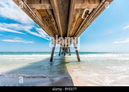 Under Okaloosa island fishing pier in Fort Walton Beach, Florida with wooden pillars green waves in Panhandle Gulf of Mexico during sunny day Stock Photo