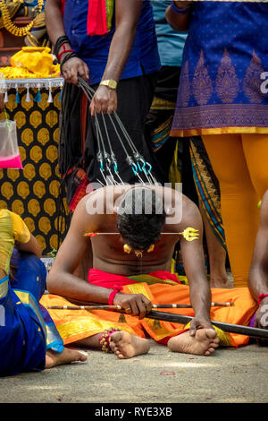 Exhausted man resting on ground with hooks pierced in his back - Thaipusam festival - Singapore Stock Photo