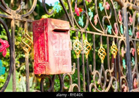 Red metal mailbox on a beautiful iron fence decorated with patterns Stock Photo